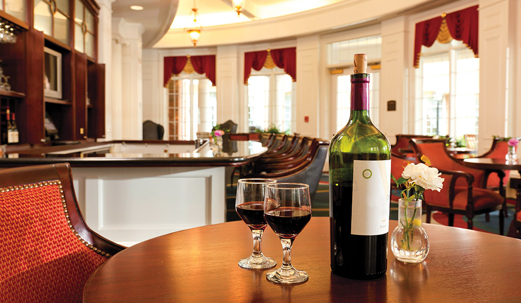 Bottle of wine with two glasses on top of a table with a bar in the background.